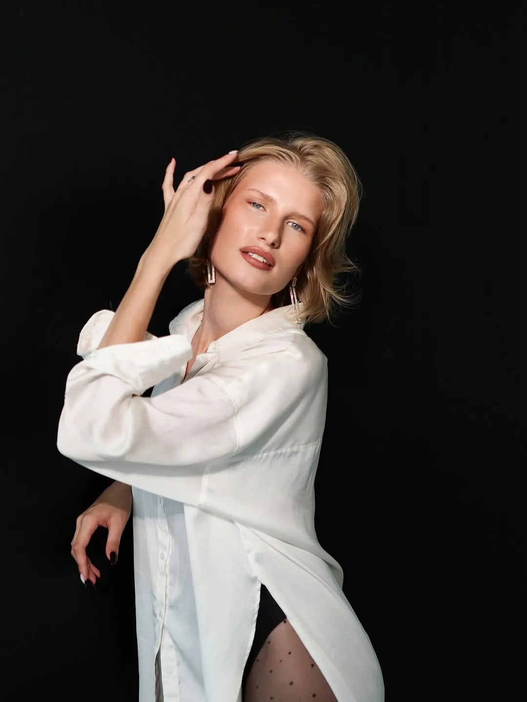 Fotosesija: modele baltā kreklā, roka pie sejas